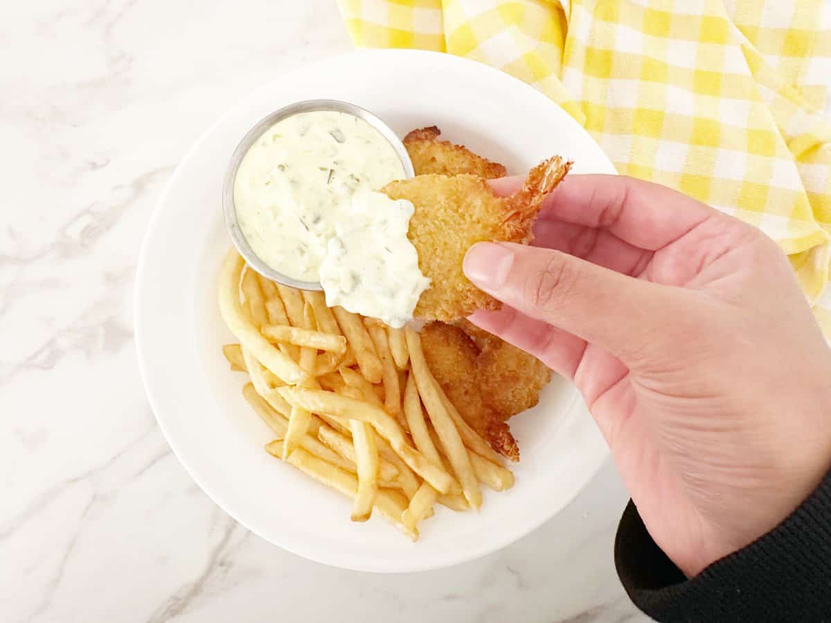 Hand holding fried shrimp dipped in tartar sauce.