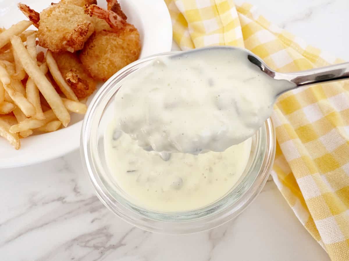 Copycat McDonalds tartar sauce dripping from a silver spoon into a jar.