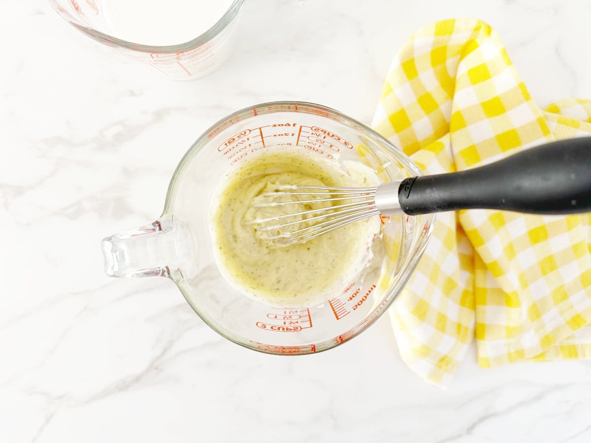 Down view of mixed mayo and ranch powder in glass measuring cup with a whisk.