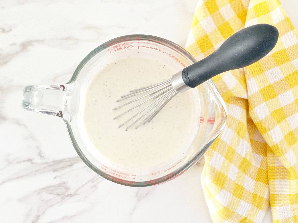 Down view of finished ranch dressing in glass measuring cup with a whisk.