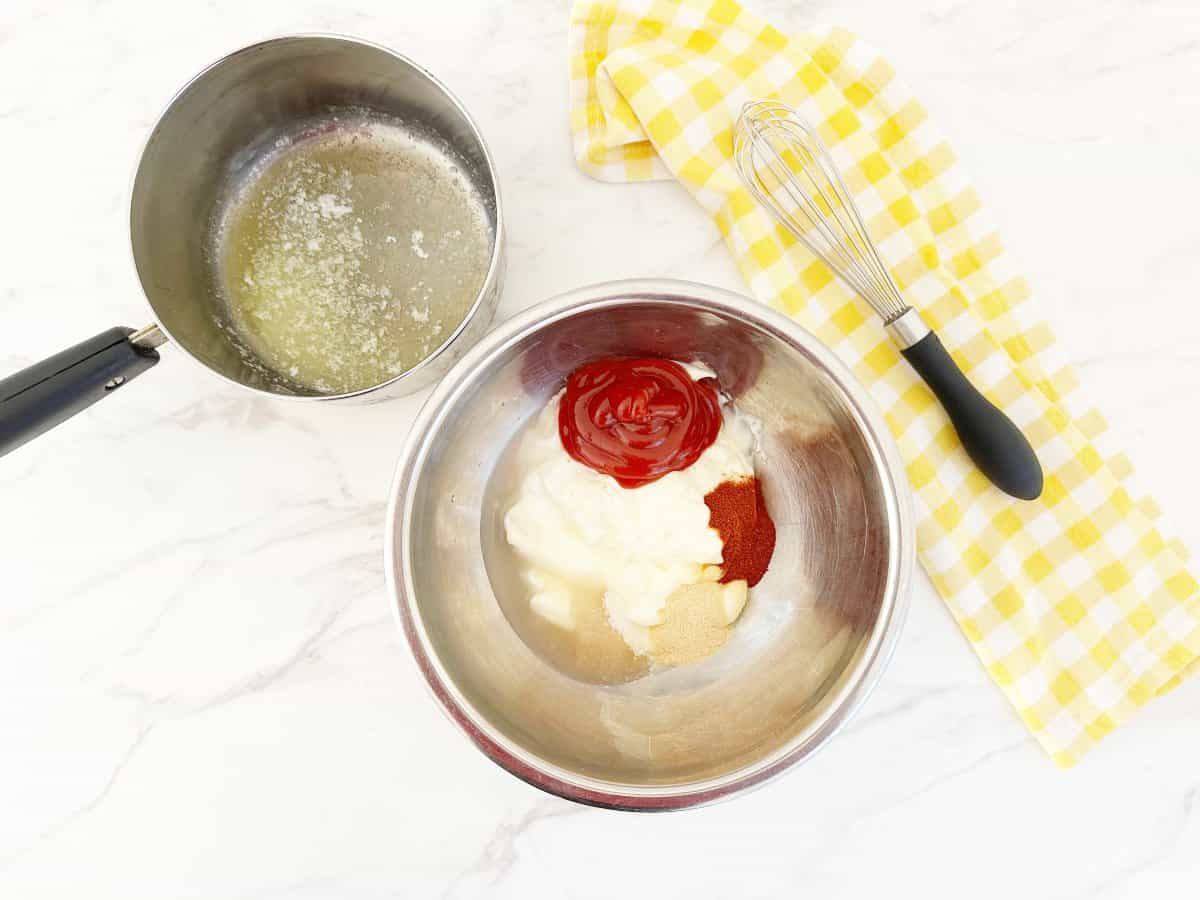 Down view of prepped yum yum sauce ingredients in silver bowl. Next to the bowl is a small pot with melted butter and a whisk.