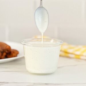 Clear jar with restaurant style ranch dressing. A spoon coated with the dressing showing the texture dripping into the jar.