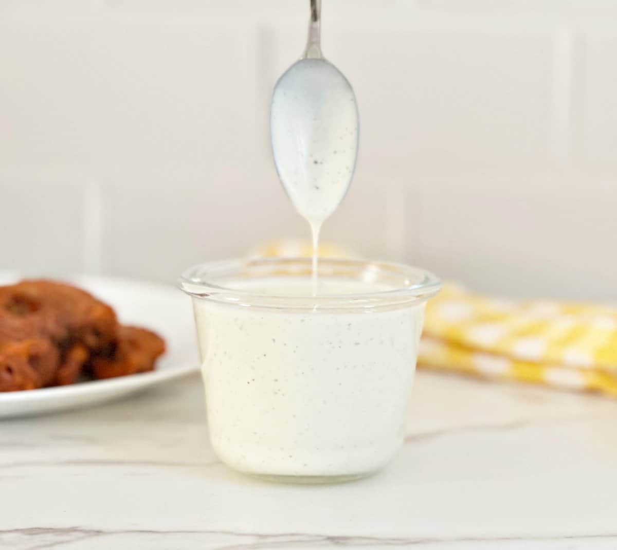Clear jar with restaurant style ranch dressing. A spoon coated with the dressing showing the texture dripping into the jar.