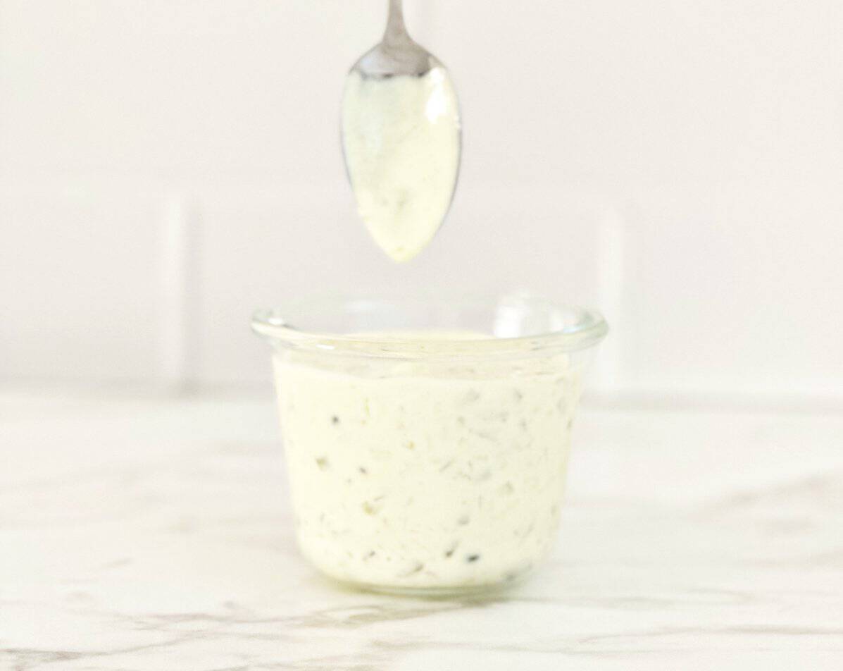 Clear jar with restaurant style tartar sauce. A spoon coated with the sauce showing the texture.