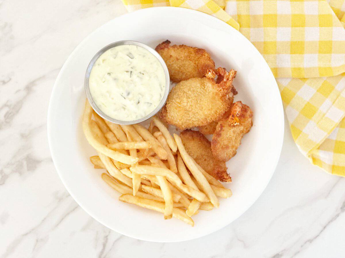 Down view of white plate with fried shrimp, French fries, and small silver bowl with tartar sauce.