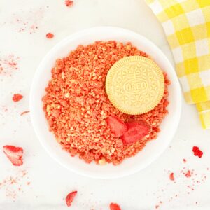 Down view strawberry crunch topping in white bowl with golden Oreo and freeze dried strawberries.