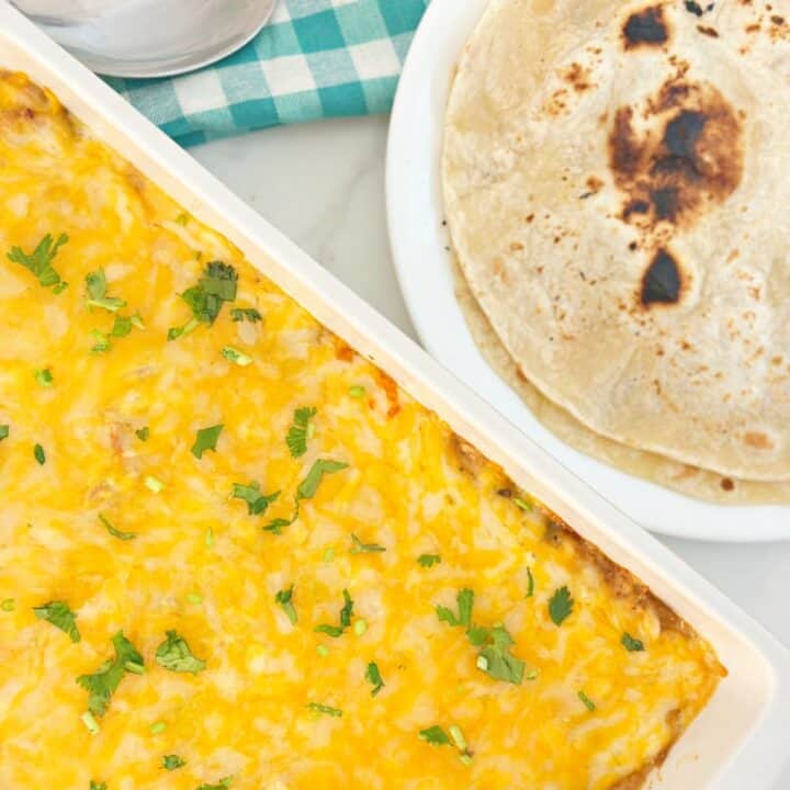Down view of white baking dish with baked chicken fajita casserole and white plate with two flour tortillas.