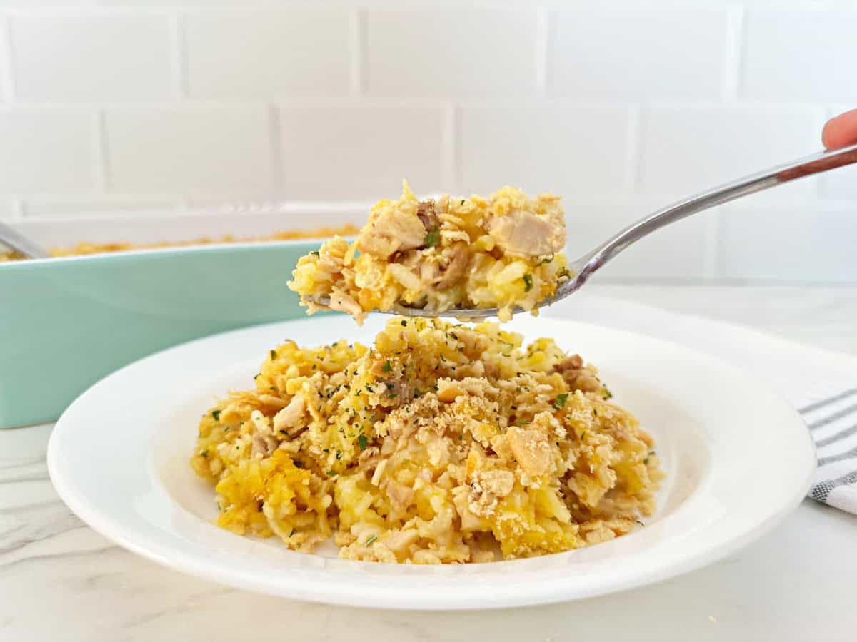 Fork holding a portion of the casserole. Under is a white dinner plate with more casserole.
