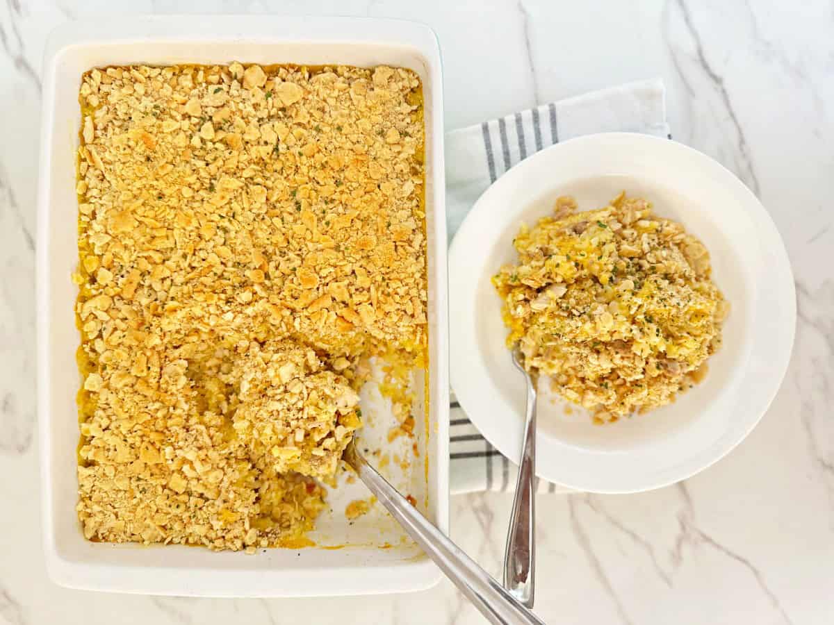 Down view of cheesy chicken casserole with rice in white baking dish. Next to a dinner serving in white plate and fork.