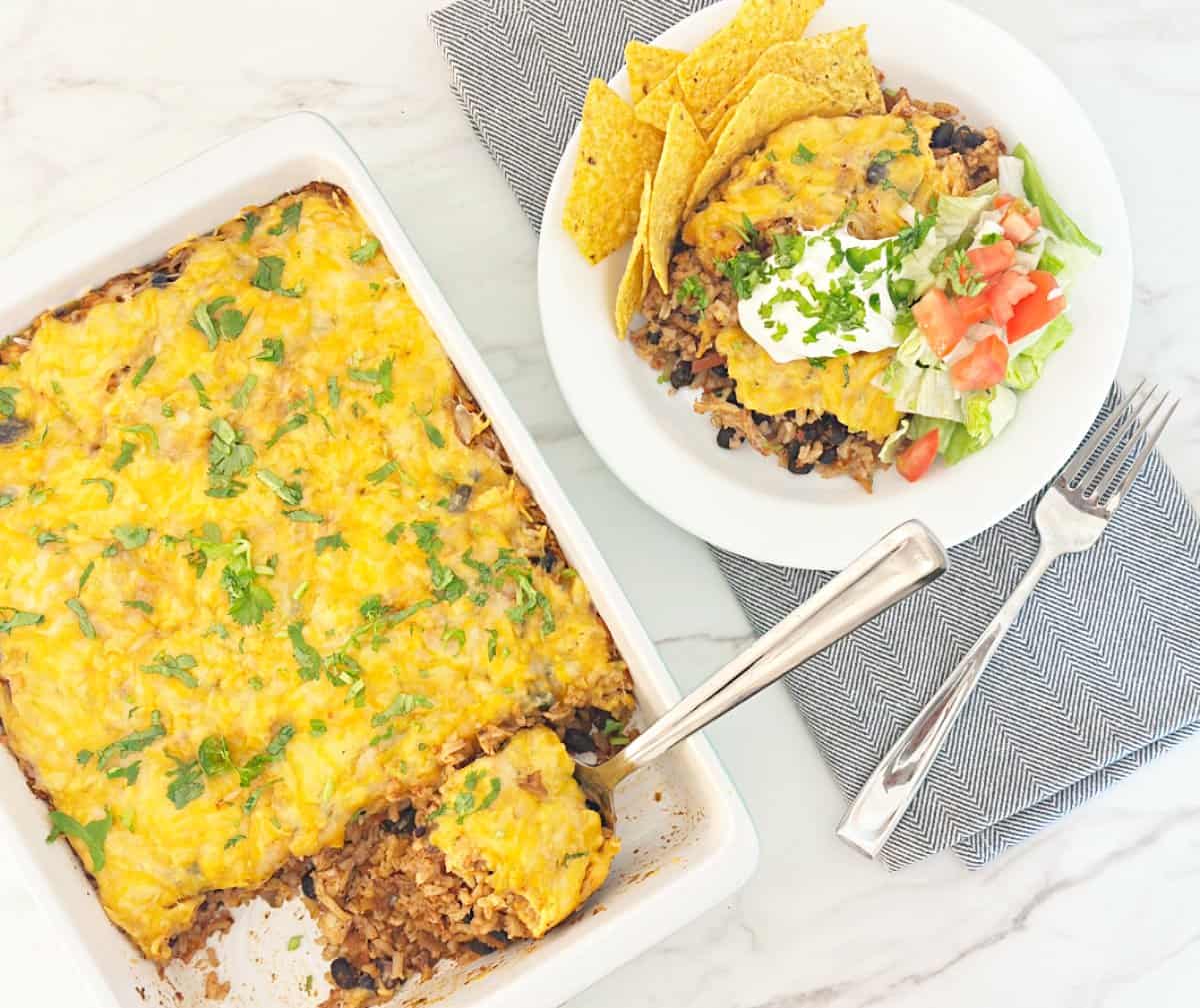 Down view of chicken mexican rice bake in casserole dish. Next to a rice bowl and fork.