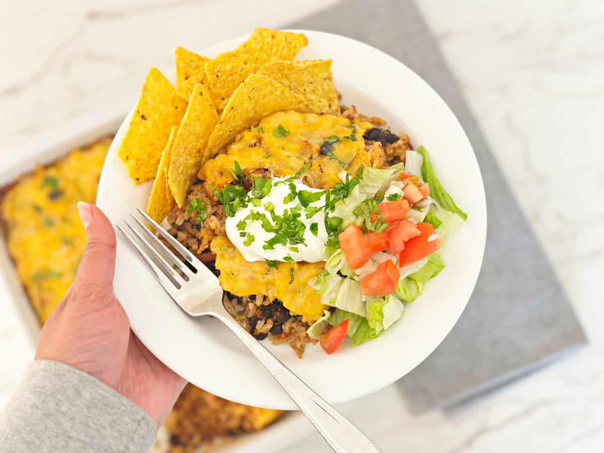 Hand holding a chicken taco rice bowl topped with sour cream and cilantro.