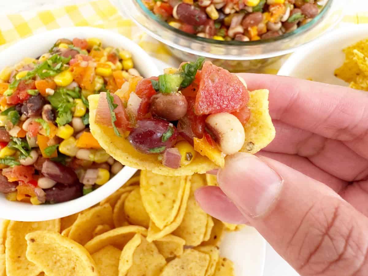 Hand holding a corn chip with cowboy caviar. Zoomed in to show all ingredients and texture.