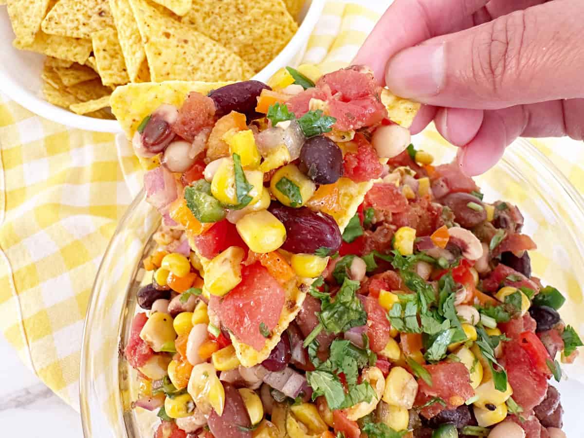Hand holding a tortilla chip with cowboy caviar.