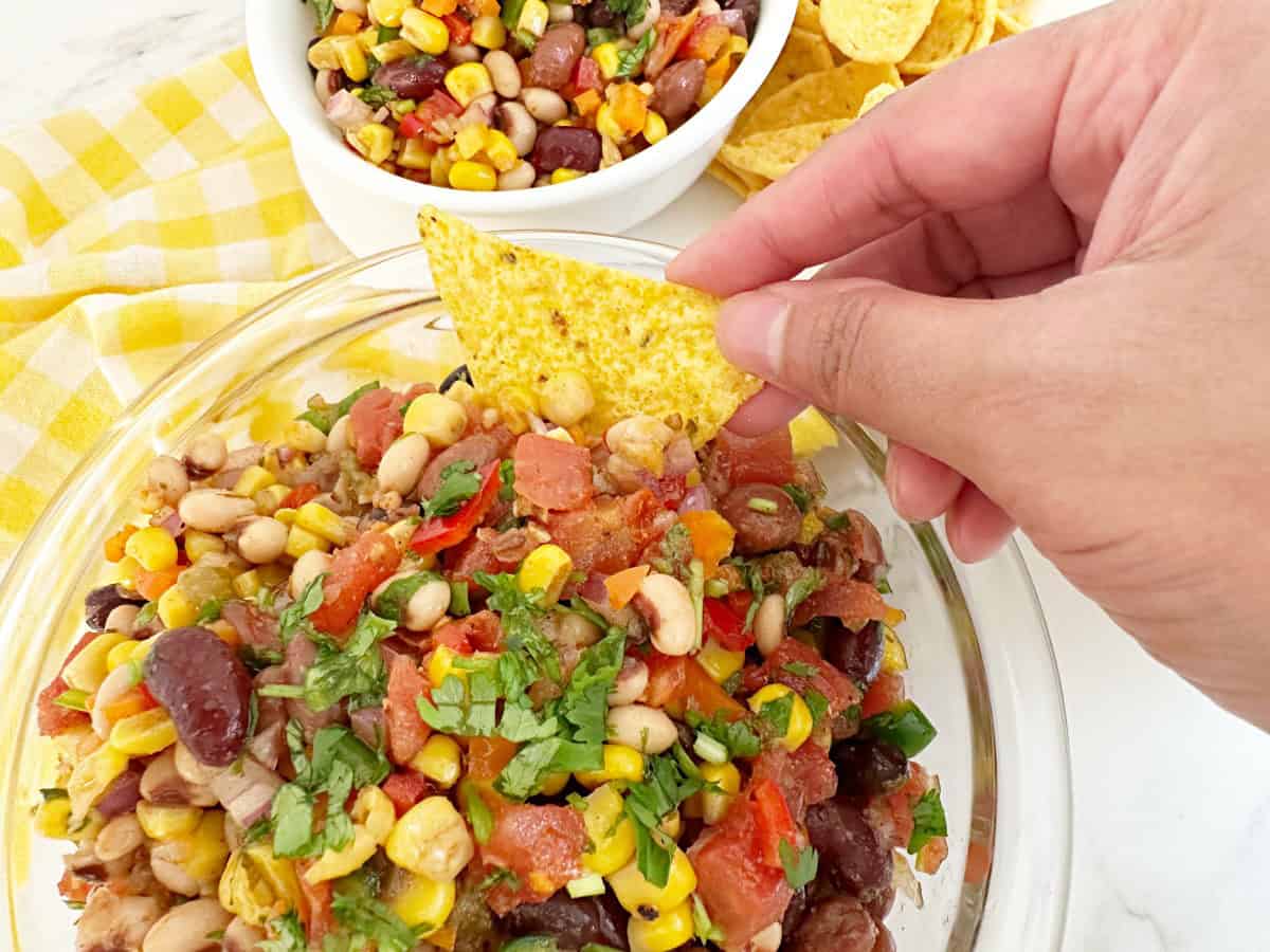 Hand dipping a tortilla chip into the in a clear serving bowl.