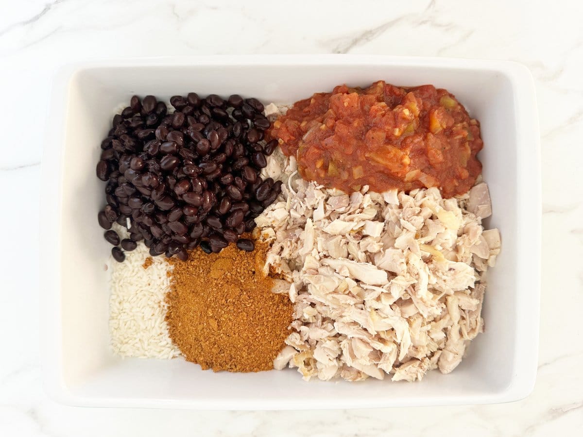 Down view white baking dish with black beans, salsa, chicken, and taco seasoning.