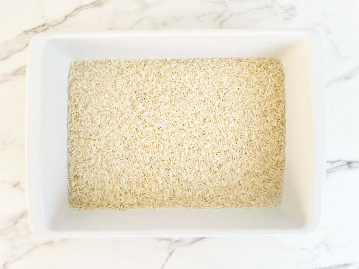 Down view white baking dish with raw long grain rice.
