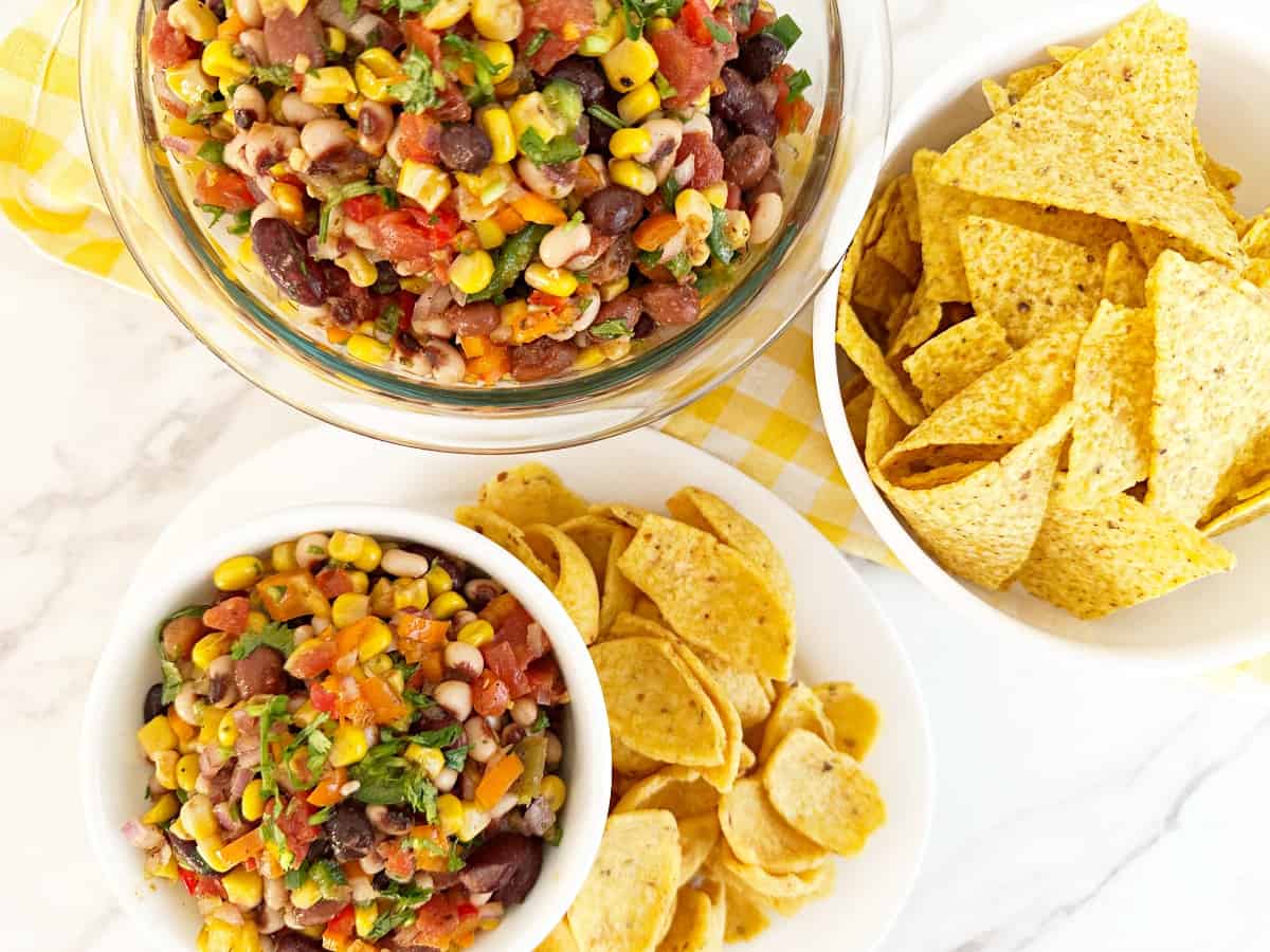 Down view of easy cowboy caviar in two bowls surrounded by tortilla chips and corn chips.