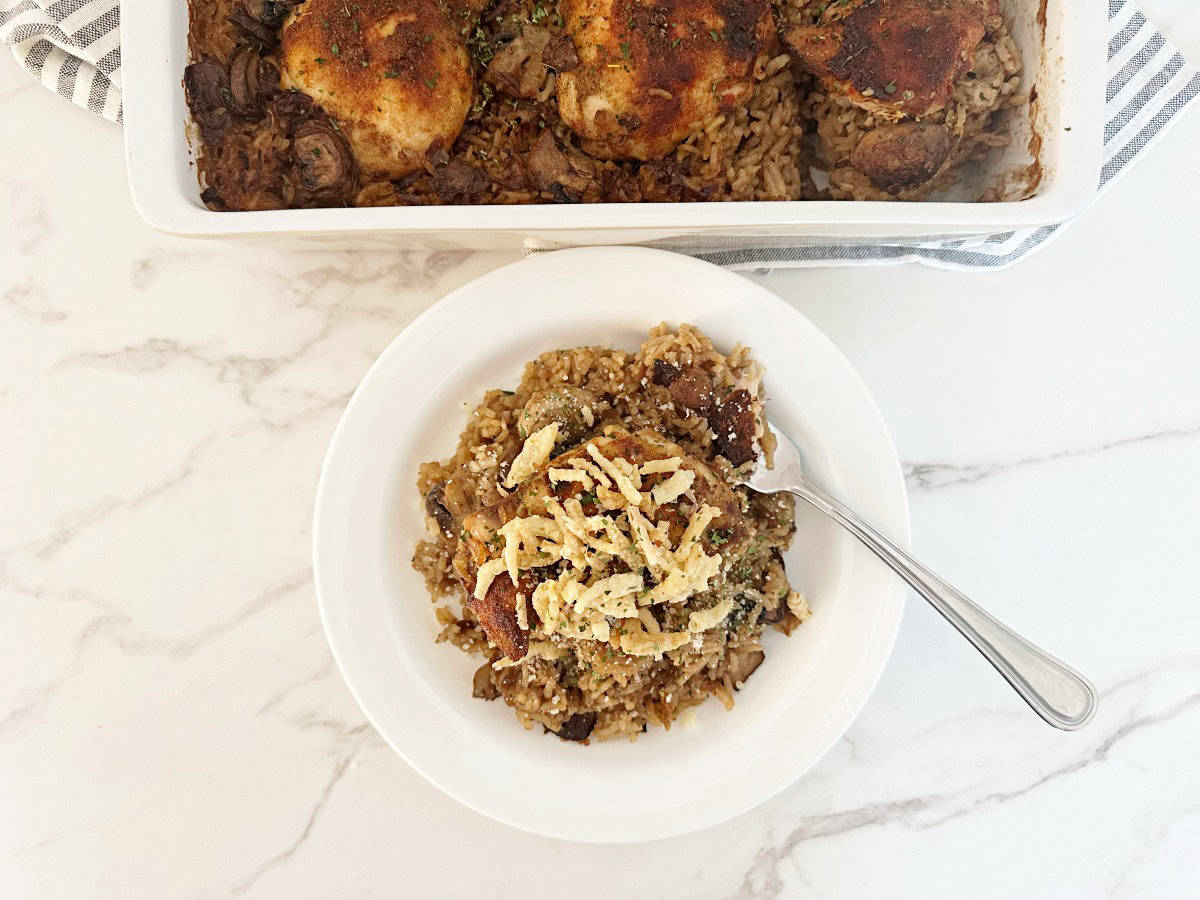 Down view of stick of butter rice and chicken with in casserole dish. Next to a serving topped with crispy fried onions in white dinner plate and fork.