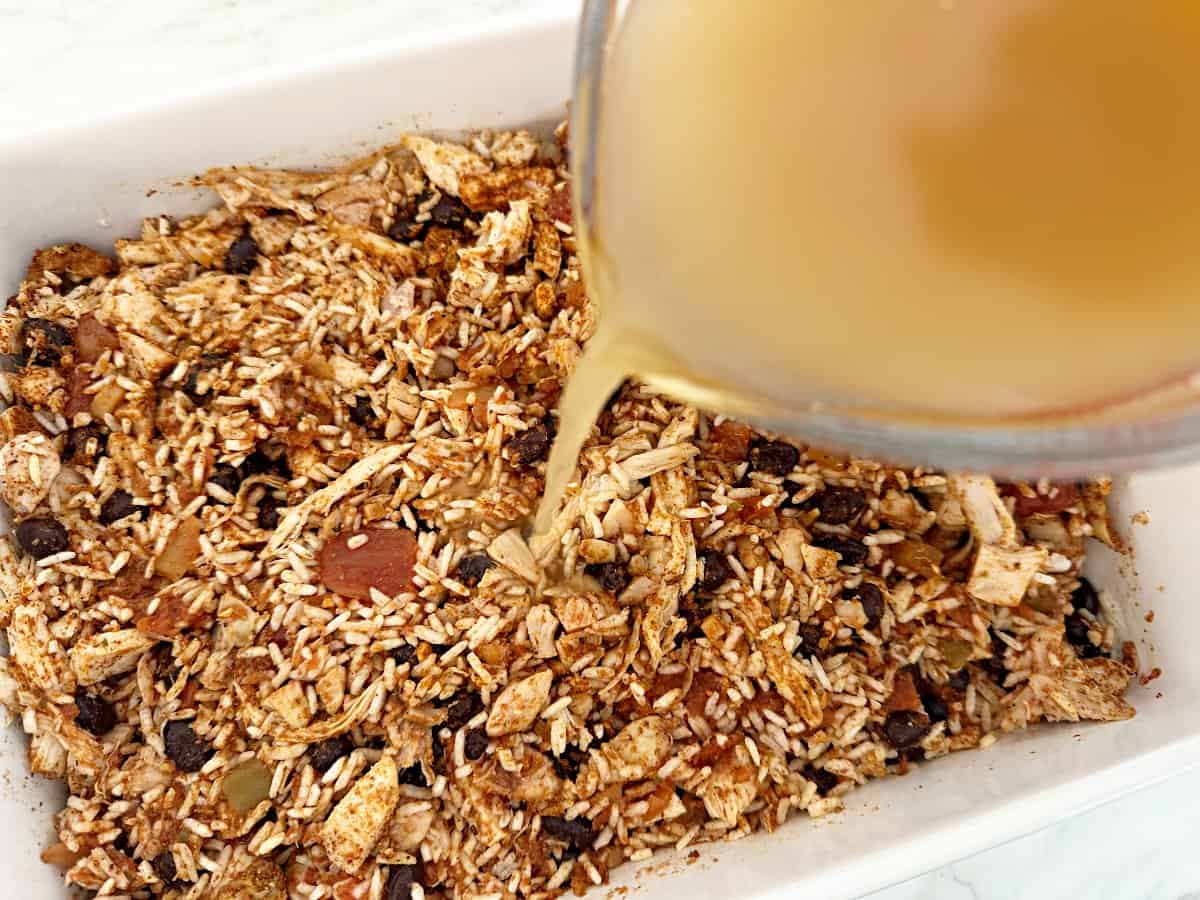 Chicken broth being poured onto mixed ingredients.