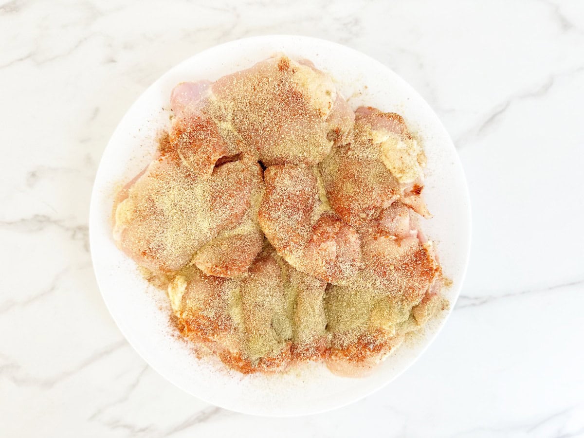 Down view of seasoned boneless chicken thighs on white plate.