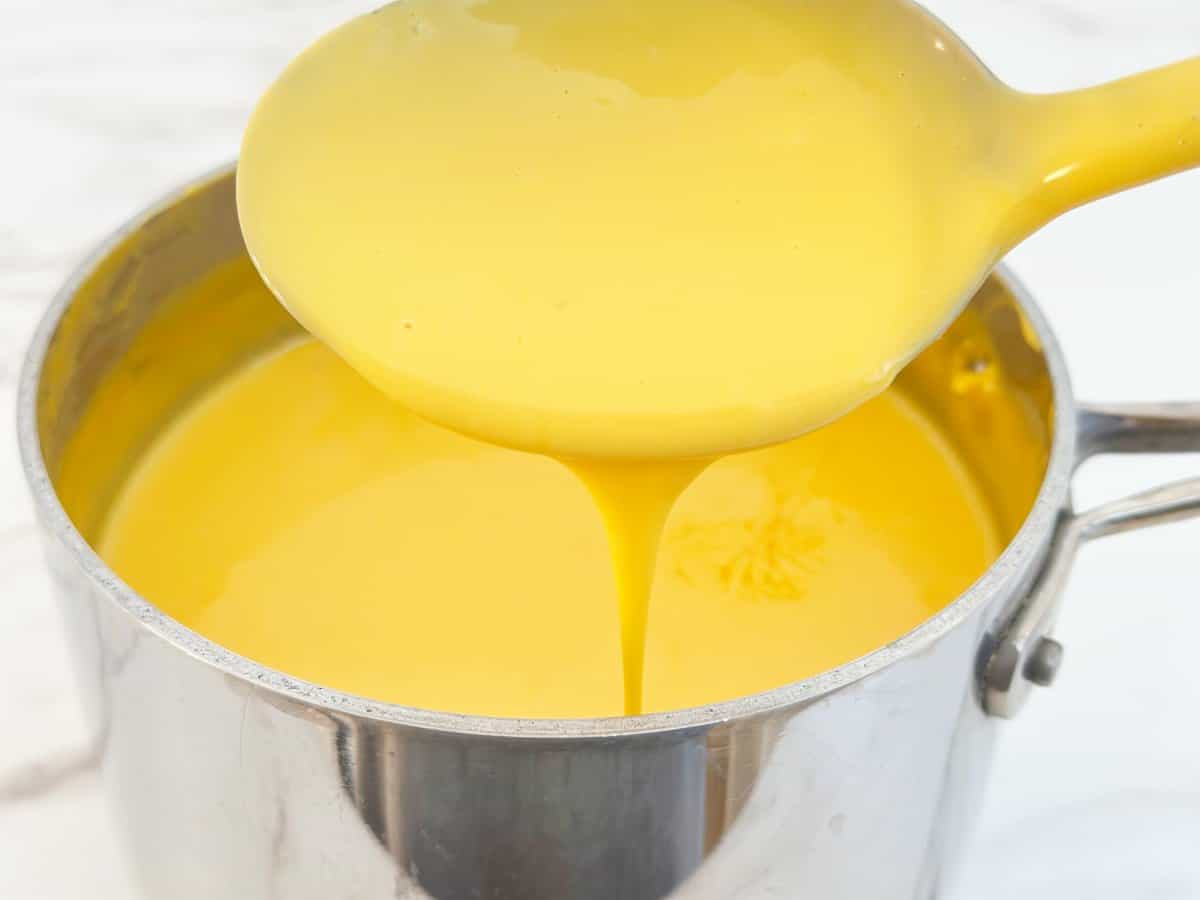 Spoon with pouring smooth cheese sauce from a saucepan.