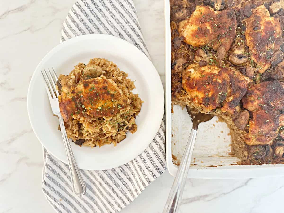 Down view of stick of butter rice and chicken in casserole dish. Next to a dinner serving in white plate and fork.