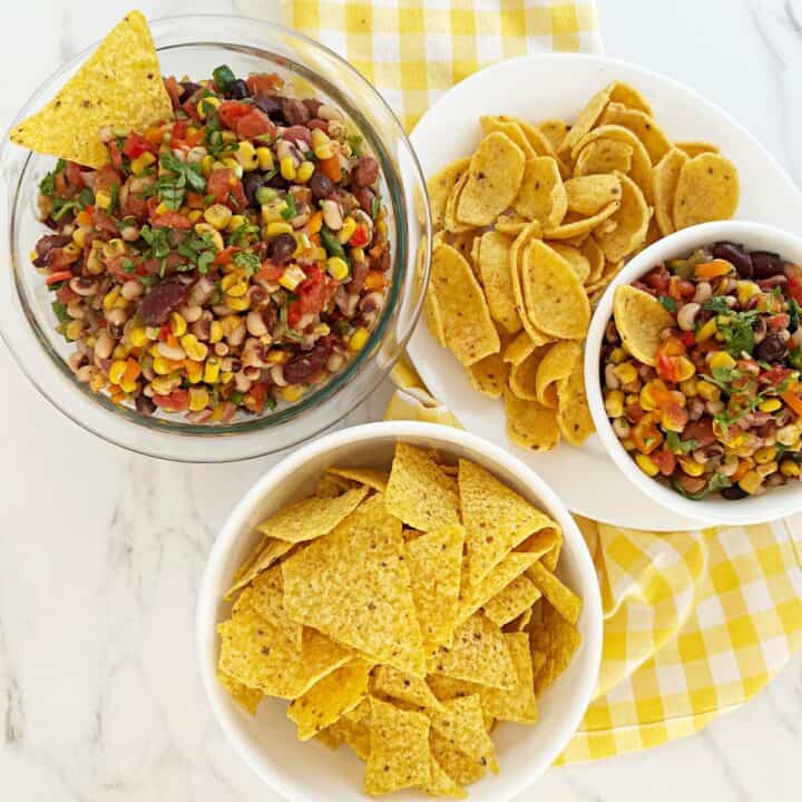 Down view of Texas cowboy caviar in two bowls surrounded by tortilla chips and corn chips.