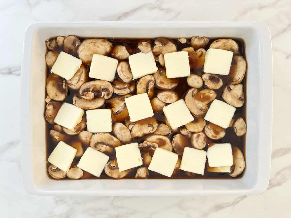 Down view white baking dish with sliced stick of butter and mushrooms.