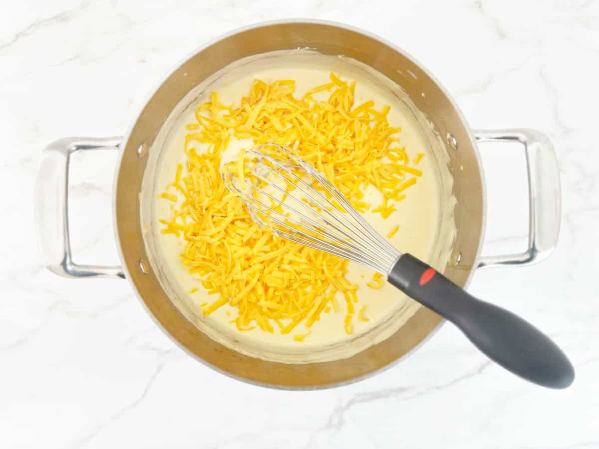 Down view of cream mixture and shredded cheese in silver pot with whisk.