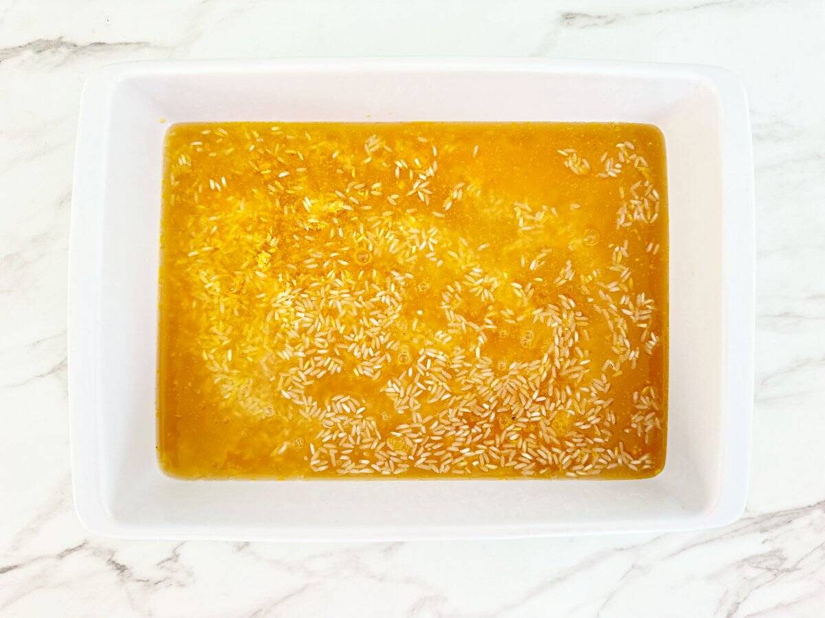 Down view white baking dish with yellow rice mix and chicken broth.