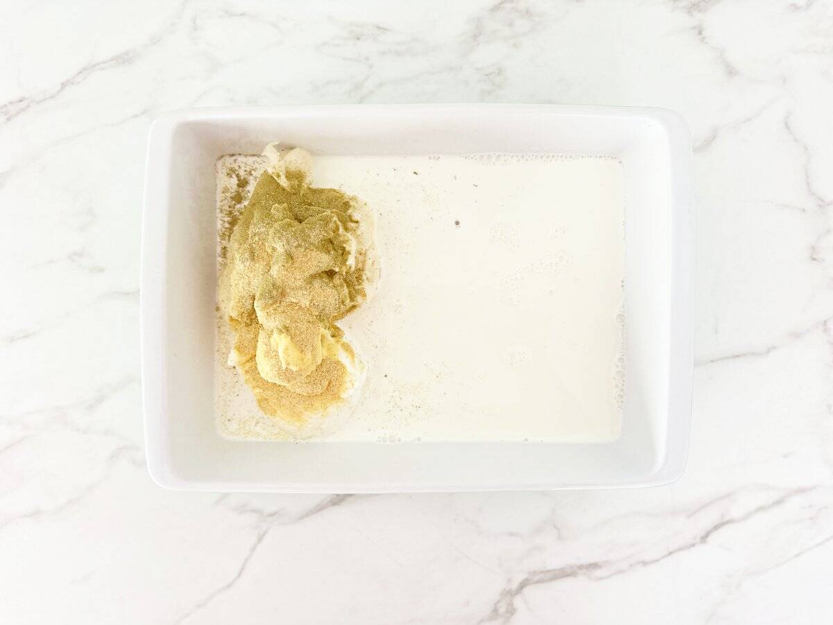 Down view baking dish with prepped condensed chicken soup, sour cream, half and half, poultry seasoning, and spices.