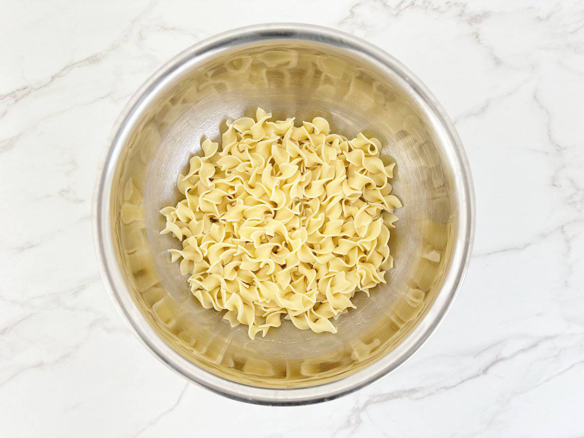 Down view silver mixing bowl with cooked egg noodles.