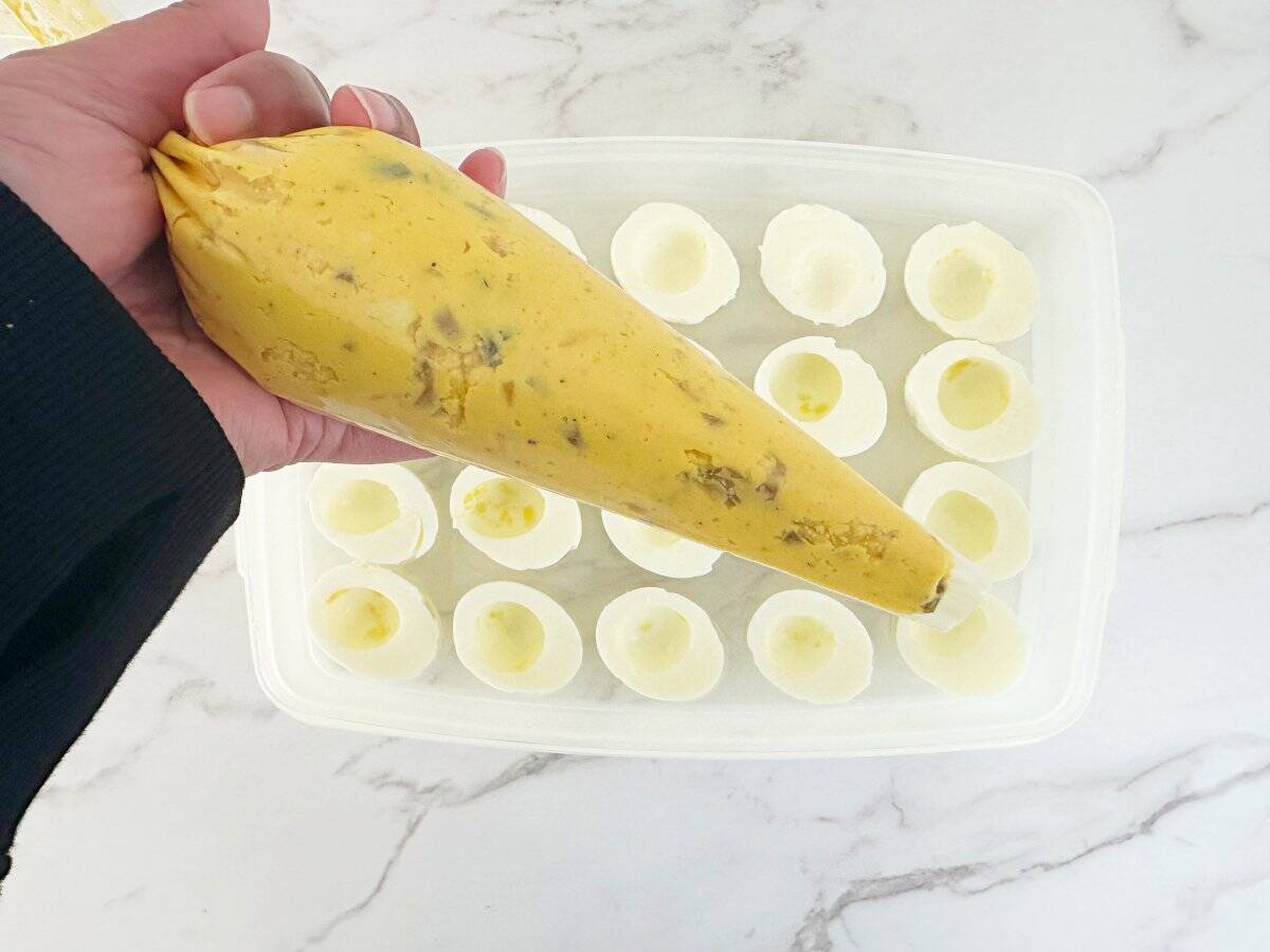 Hand holding a clear piping bag with deviled egg yolk mixture.
