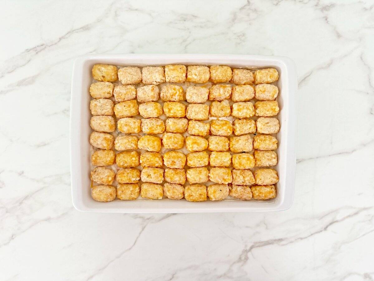 Down view of unbaked casserole topped with frozen tater tots in white baking dish.