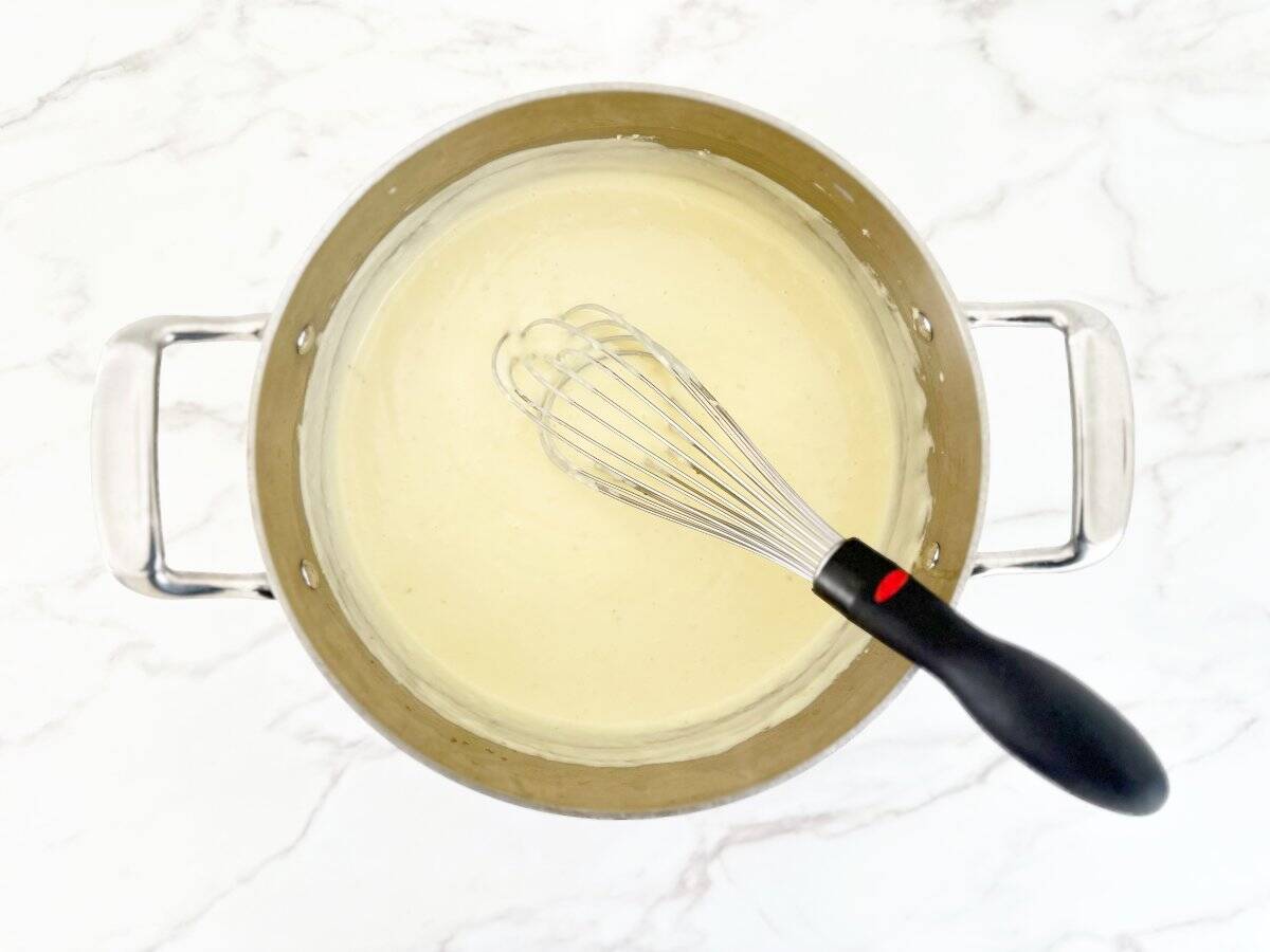 Down view of cream mixture in silver pot with whisk.