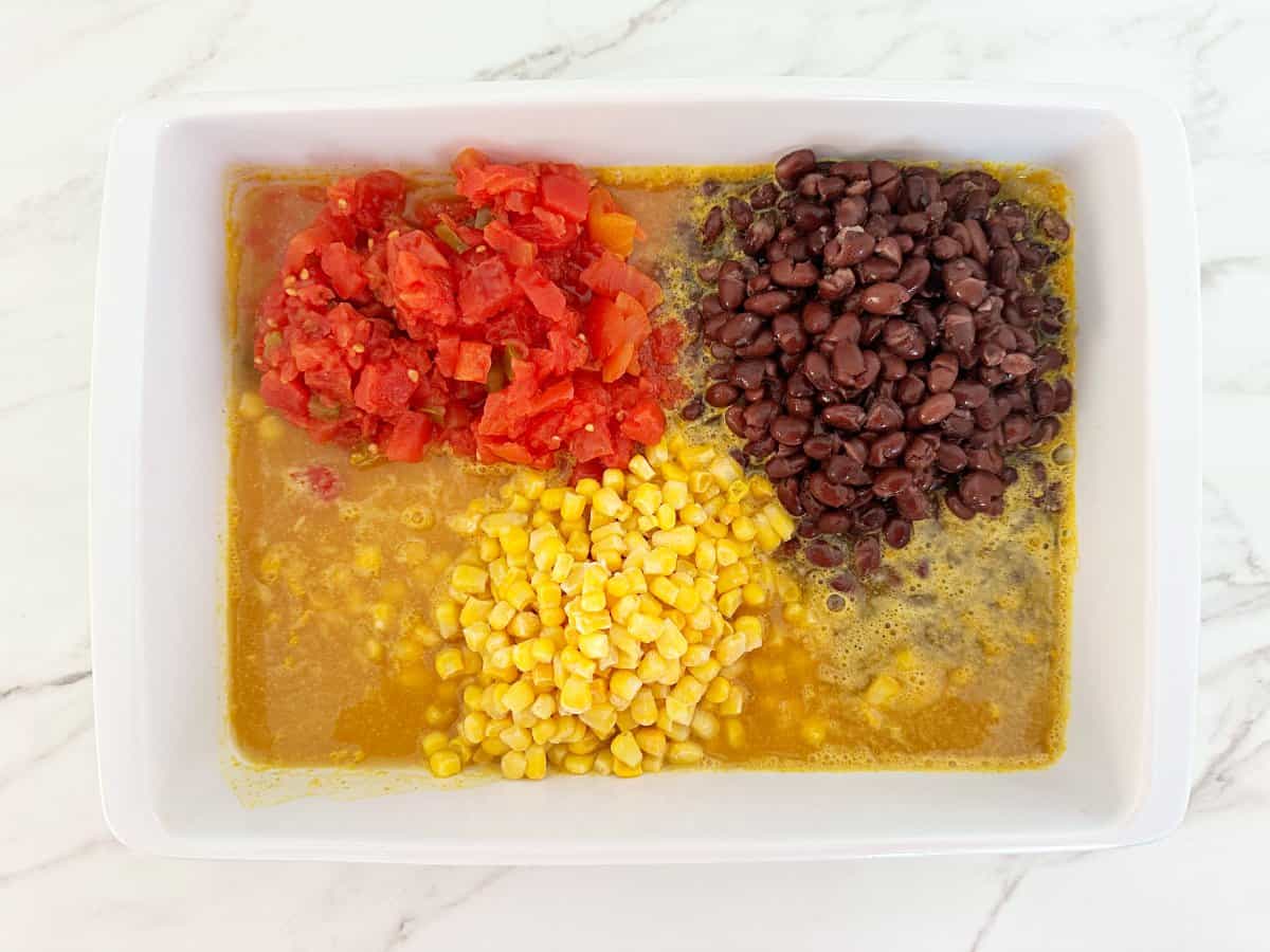 Down view white baking dish with black beans, rotel, corn, yellow rice and chicken broth.
