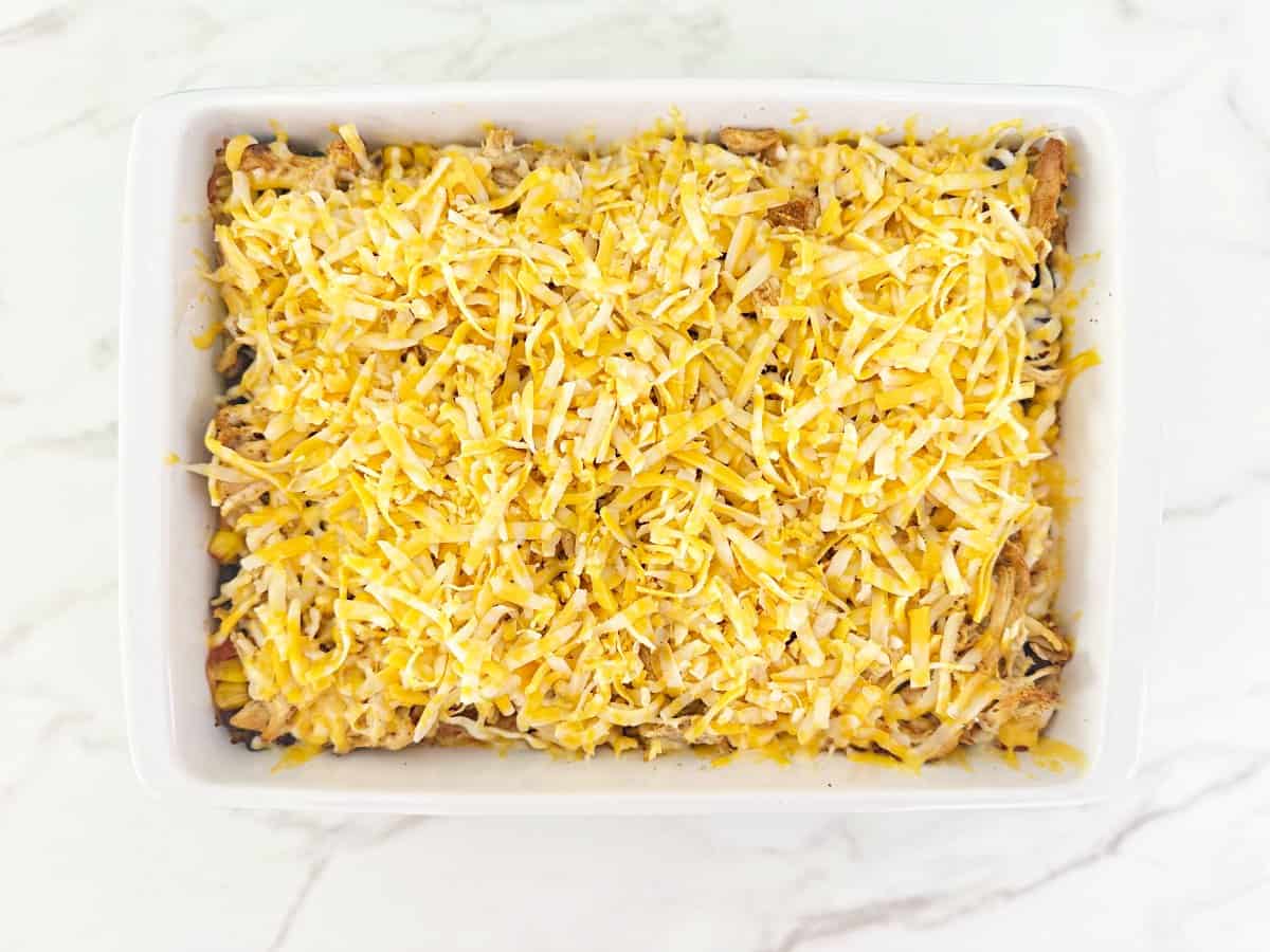 Down view of unbaked casserole topped with shredded cheese in white baking dish.