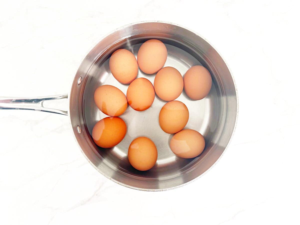 Down view of a saucepan with water and brown eggs.