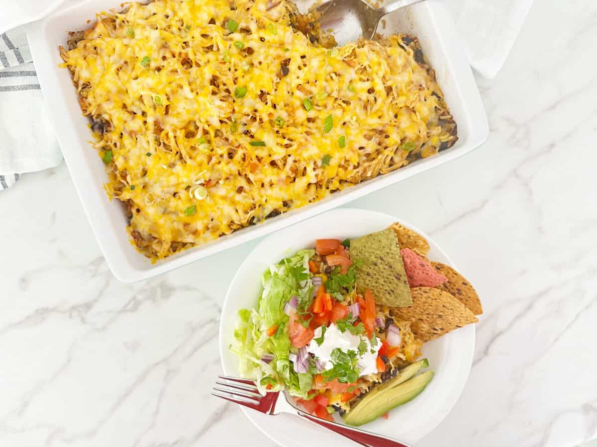 Down view of cheesy mexican chicken rice bake in casserole dish. Next to a chicken rice bowl and fork.