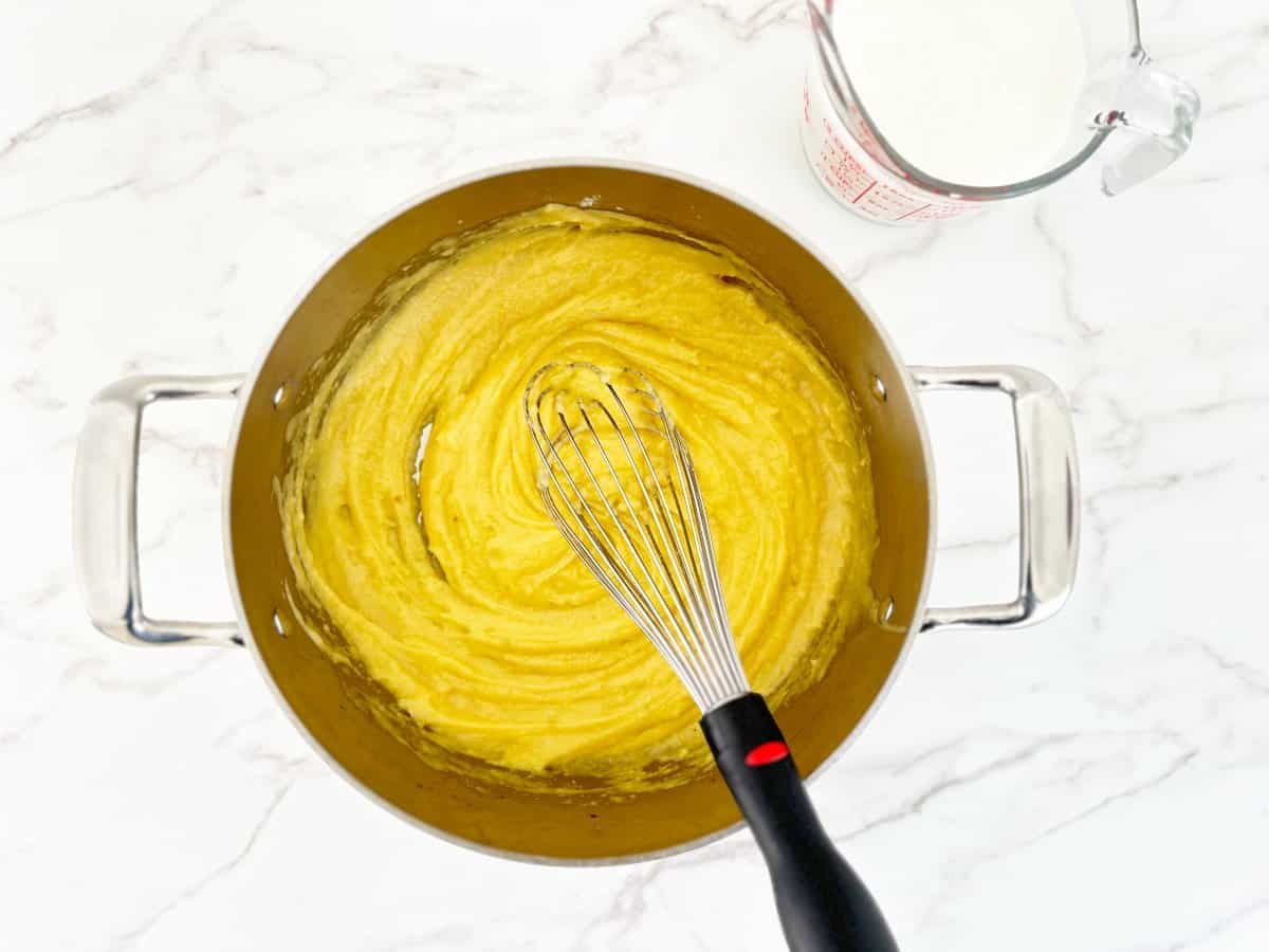 Down view of butter, flour, and broth mixture in silver pot with whisk.