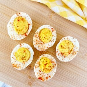 Down view of deviled eggs with paprika and relish on wood cutting board.
