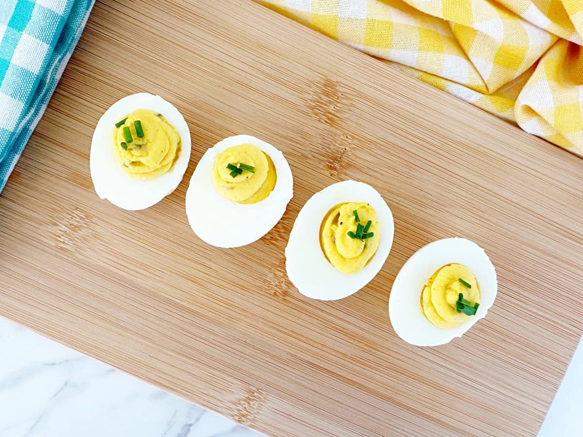 Down view of four deviled eggs with chives on wood cutting board.