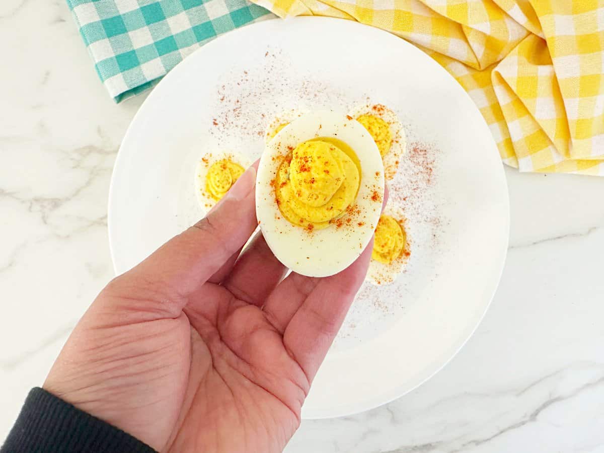 Close up view of a hand holding a deviled egg with paprika and relish.