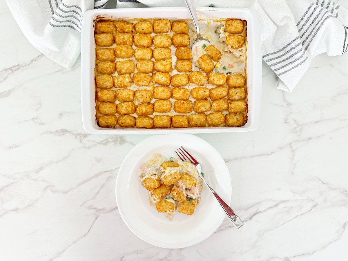 Down view of dump and bake chicken pot pie with tater tots in white baking dish. Next to a dinner serving of the casserole in white plate and fork.