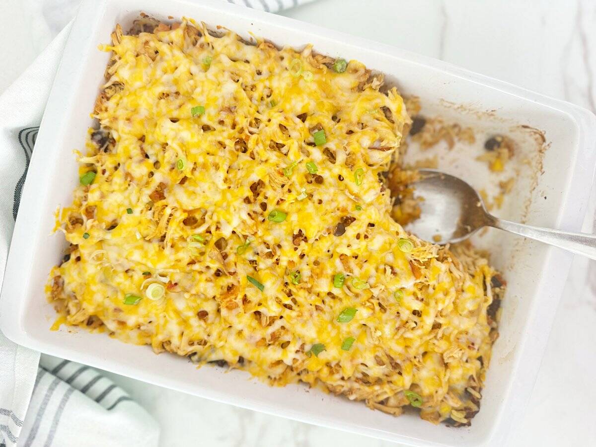 Down view of easy chicken and yellow rice casserole in white baking dish with serving spoon.