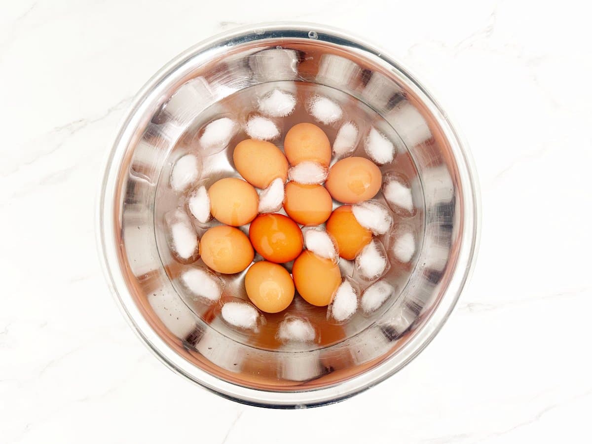 Down view of silver bowl with hard boiled eggs in ice bath.