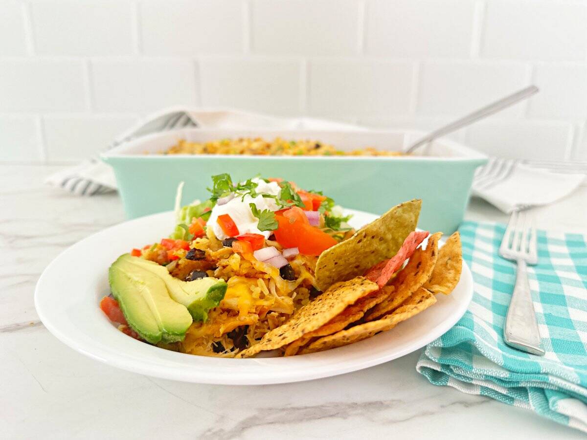 Side view chicken rice bowl topped with sour cream, tomatoes and cilantro. Side of avocado and tortilla chips.