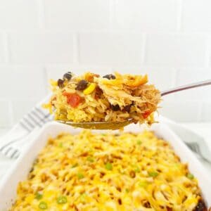 Serving spoon holding a portion of Mexican chicken rice casserole with yellow rice.