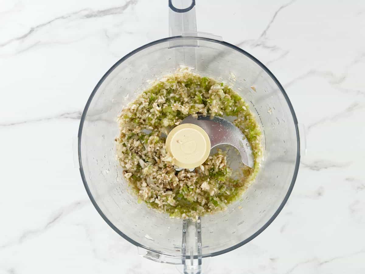 Down view of small pieces of vegetables in food processor bowl.