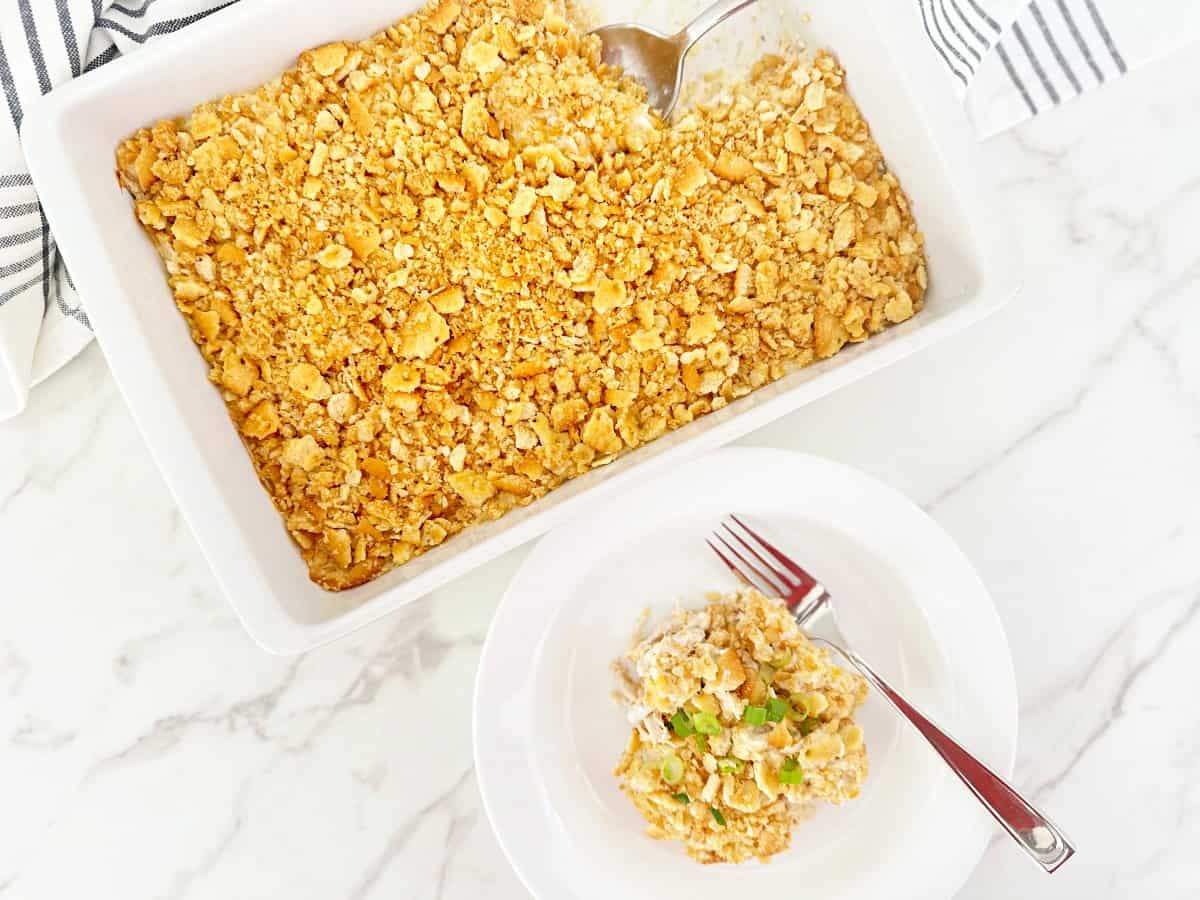 Down view of ritz cracker chicken casserole in white baking dish. Next to a dinner serving in white plate and fork.